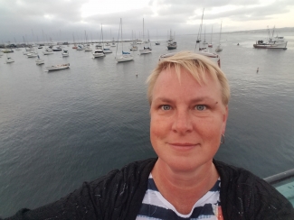 Tara Jensen standing at the edge of a body of water with sailboats in the background